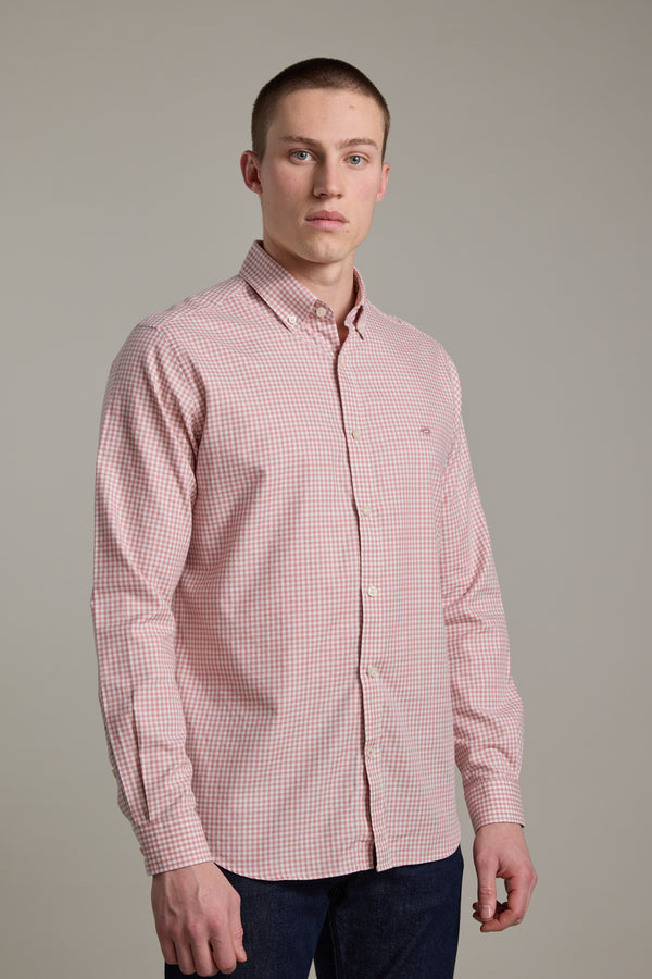 A young man with short hair and a neutral expression stands against a plain background, wearing the Barkers Courtland Check Shirt in light pink and white check, paired with dark blue jeans, looking directly at the camera.