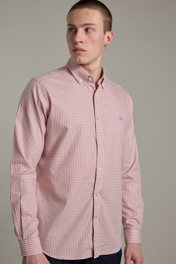 A young man wears a pink and white Barkers Courtland Check Shirt, made from responsibly sourced cotton, standing slightly turned and looking left against a plain gray background.