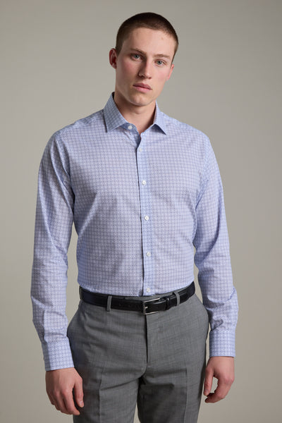 A young man with short hair stands facing forward in a Barkers Seton Print Business Shirt, tucked into gray dress pants with a black belt. He has a neutral expression and is posed against a plain light background.
