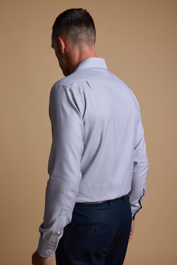 A man stands with his back to the camera, showcasing the Barkers Eaton Jacquard Business Shirt in light blue and dark trousers against a plain beige background.
