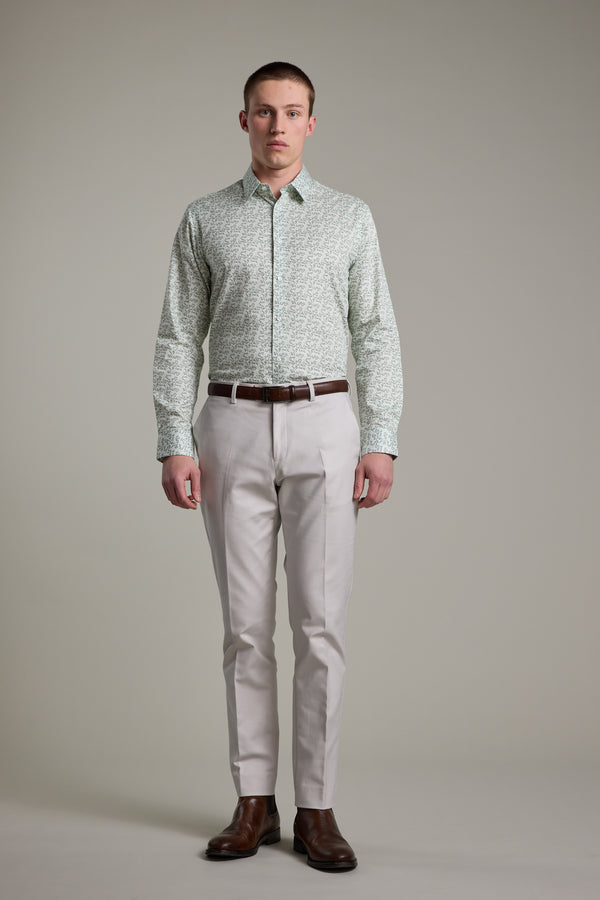 A man faces forward against a plain background, wearing the Barkers Ambrose Print Shirt in light green, made from responsibly sourced cotton, paired with light beige trousers, a brown belt, and brown dress shoes.
