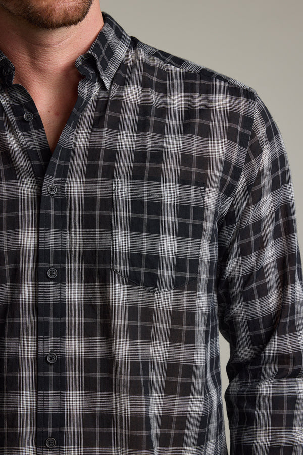 A person is shown from shoulders to mid-torso wearing the Barkers Carter Check Shirt, a lightweight long-sleeve shirt featuring a black and white plaid pattern, with part of the face visible against a neutral background.