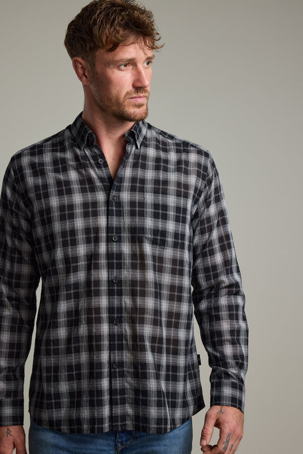 A man with short brown hair and a beard wears the Barkers Carter Check Shirt in black, white, and gray with blue jeans, looking to the side against a neutral background.