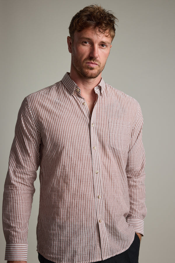 A man with short, tousled hair wears the Barkers Sumter Stripe Shirt, a lightweight long sleeve featuring vertical pink and white stripes. He stands against a plain light gray background, gazing neutrally at the camera.