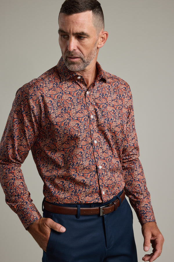 A man wearing the Barkers Paisley Business Shirt in a classic fit with a red and blue pattern, paired with navy pants and a brown belt. Crafted from Eco Easy Care fabric for effortless style.
