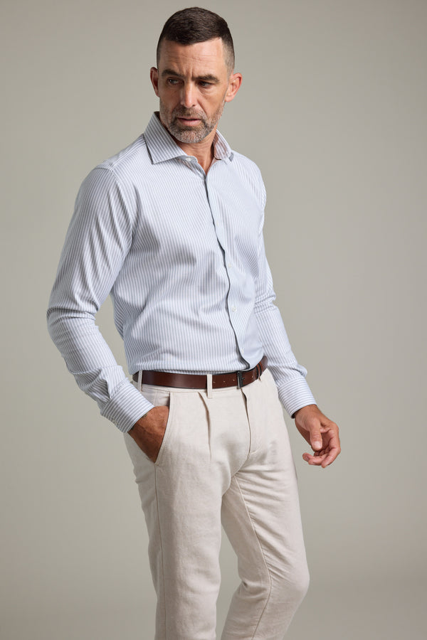 A man with short hair and a trimmed beard wears the Barkers Clarke Stripe Business Shirt tucked into beige trousers with a brown belt, standing with one hand in his pocket against a plain background.