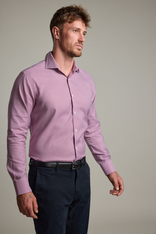 A man with short hair and a beard wears the Barkers Mitchel Check Business Shirt, tailored fit, in pink check pattern, paired with dark trousers. He stands against a plain light background, facing slightly right with a neutral expression.