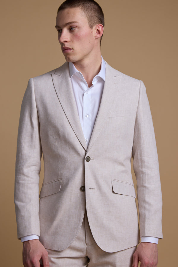 A person models the Barkers Somerton Linen Blazer over a white dress shirt, standing against a plain tan background and looking left with a neutral expression—an ideal look for summer weddings.