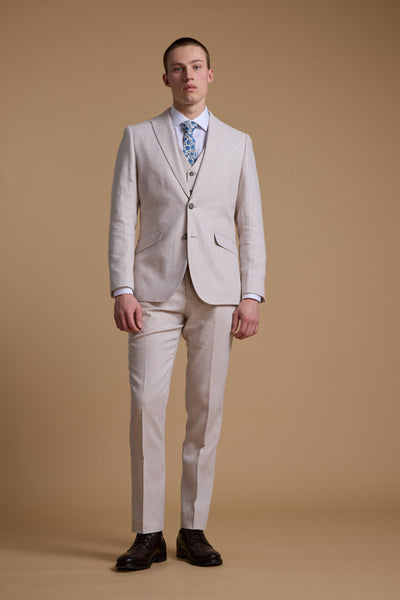 A person stands against a beige background, wearing the Barkers Somerton Linen Blazer—a light beige, tailored-fit style ideal for summer weddings—paired with a vest, white shirt, blue patterned tie, and dark brown dress shoes.
