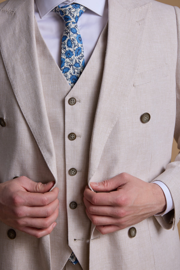 A person wears a cream men's 3-piece suit with a blue floral tie and the Barkers Somerton Texture Waistcoat, buttoning the jacket. Only the torso and hands are visible—a refined example of summer tailoring.