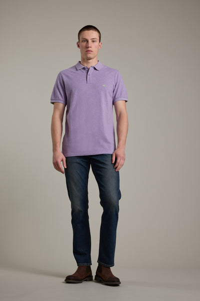 A man stands facing forward against a plain background, wearing a Barkers Regent Pique Polo in light purple, dark blue jeans, and brown shoes.