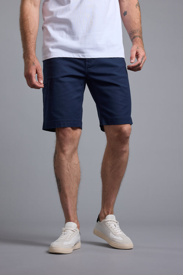 A man wearing Barkers Anvil 5Pkt Short, paired with a white T-shirt and white sneakers, stands against a plain gray background. His face is not visible in the image.