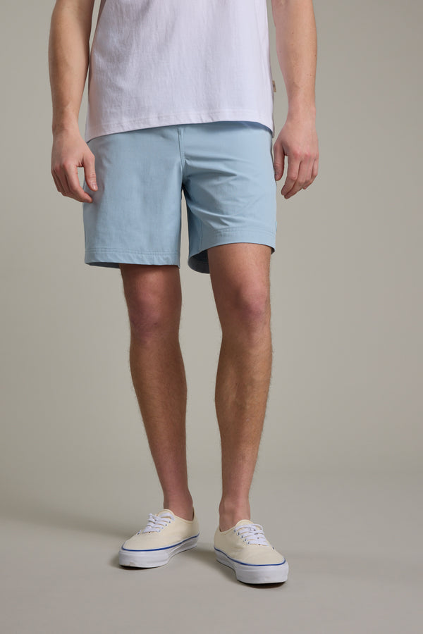 A person wearing a white T-shirt, Barkers Davis Weekend Short in light blue, and white sneakers stands against a plain light gray background with their hands relaxed by their sides.