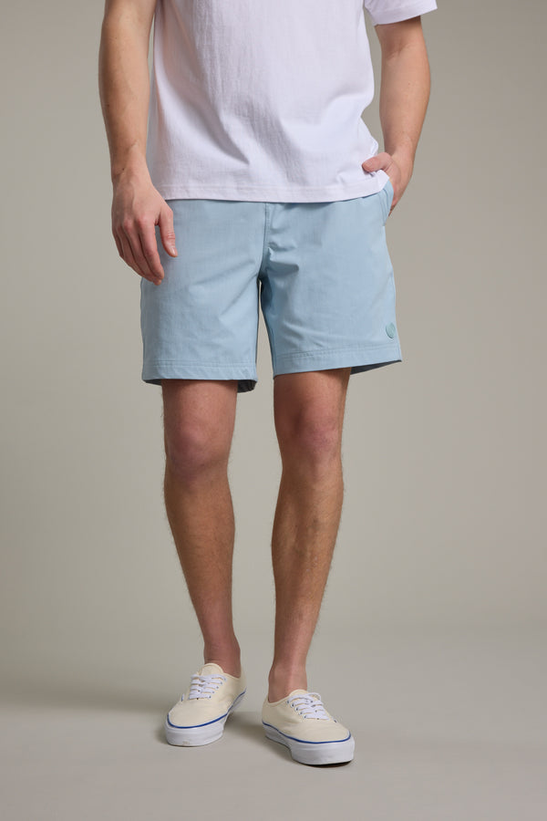A person wearing a white t-shirt, Barkers Davis Weekend Short in light blue, and white sneakers stands with one hand in their pocket against a neutral background. Their face is not visible.