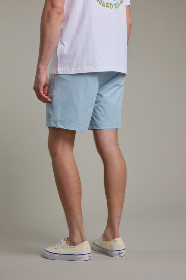 A person, shown from the waist down against a plain background, models Barkers’ Davis Weekend Short in light blue, paired with a white t-shirt and cream sneakers.