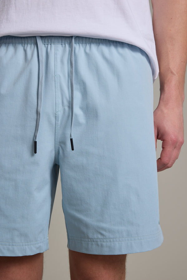 A person wearing Barkers Davis Weekend Short in light blue recycled polyester and a white t-shirt, shown from waist to mid-thigh, with their right arm partially visible by their side.