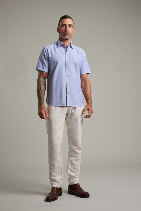 Man in Barkers Archer Oxford Shirt, beige pants, and brown boots stands.