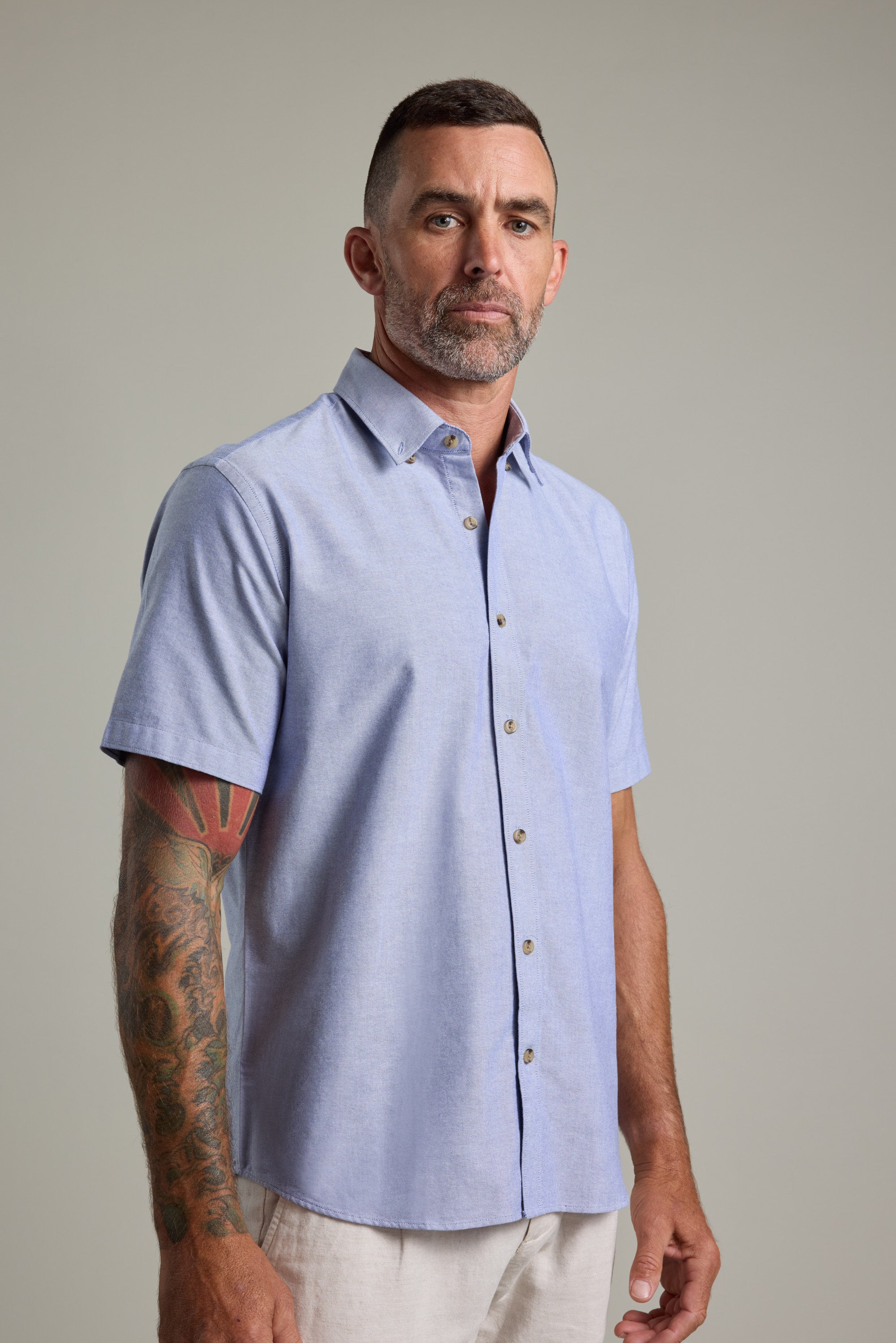 Man with short hair and tattoos wears a light blue Barkers Archer Oxford Shirt.