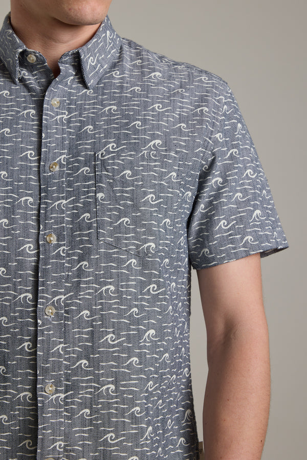 A person wears the Barkers Shelby Print Shirt, a short sleeve summer shirt made from responsibly sourced cotton with a blue and white wave pattern, shown from shoulders to mid-torso against a plain background.