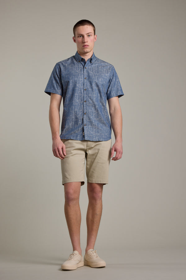 A man faces forward with a neutral expression, wearing the Barkers Yacht Jacquard Shirt against a plain background. He pairs the blue patterned summer shirt with beige shorts and light-colored sneakers.