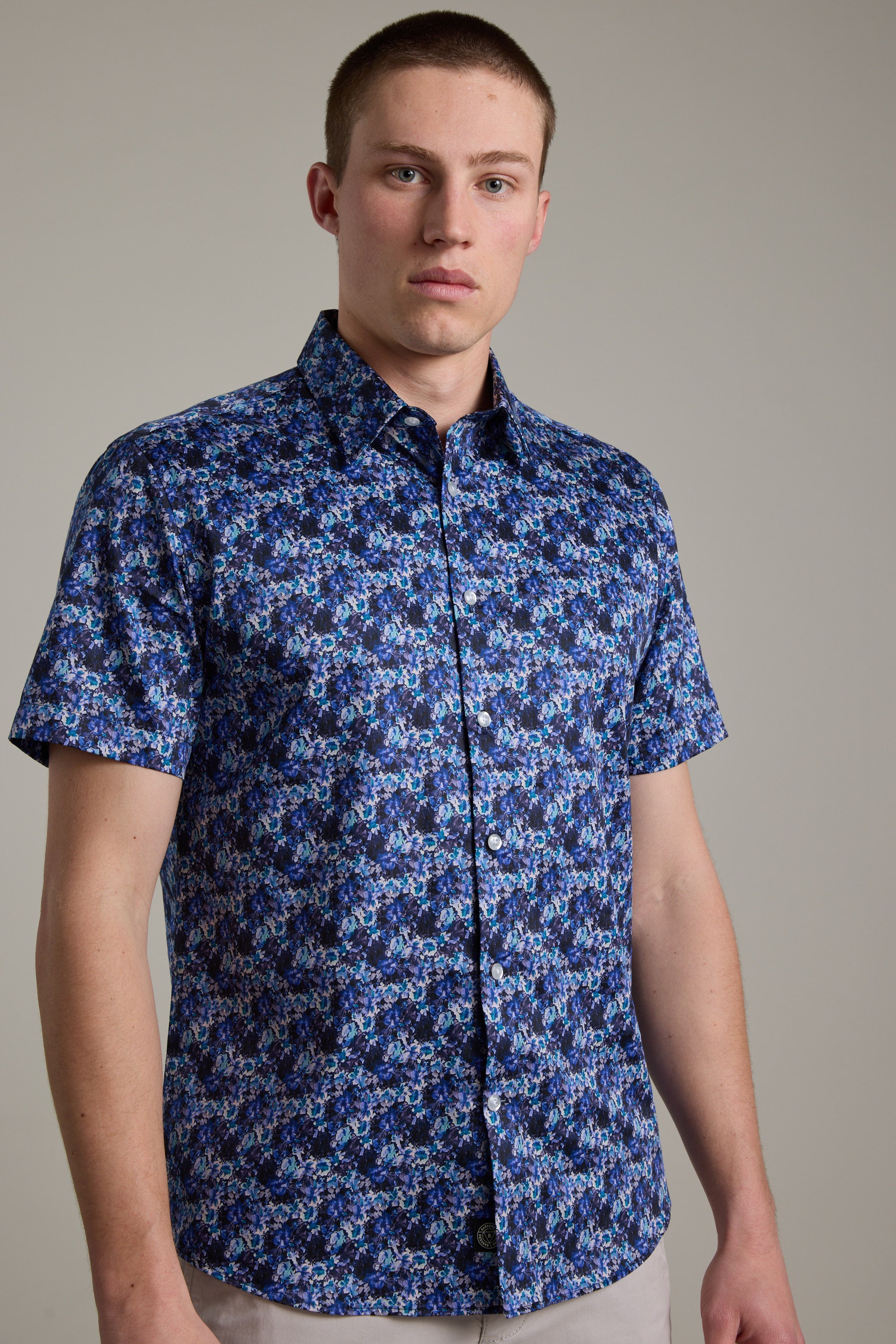 A person wearing the Barkers Lawson Print Shirt, a short-sleeve, button-up ditsy floral shirt made from responsibly sourced cotton, stands against a plain light background.