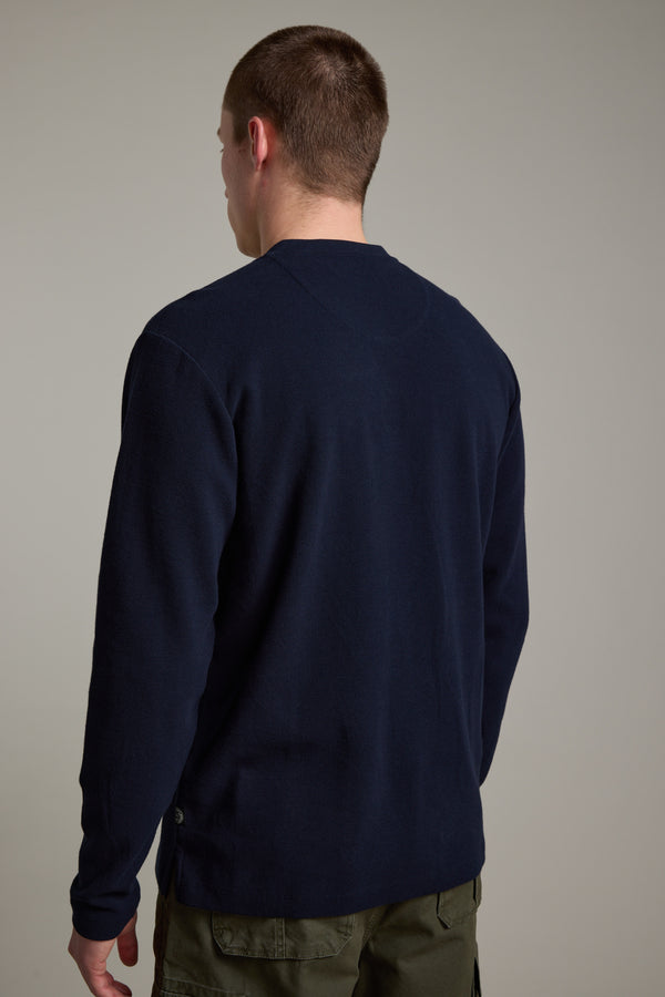 A person with short brown hair, seen from the back against a neutral background, wears Barkers’ Avenue Waffle Henley in dark navy with olive green pants.