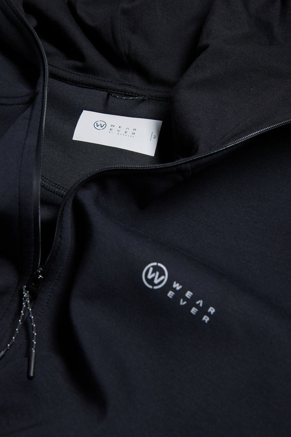 Close-up of the WearEver Altitude Hoody, a black tech fleece hoodie with zipper, WEAREVER logo on the chest, and a matching white logo label inside the collar—perfect for everyday wear.