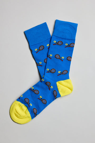 The Barkers Centre Court Tennis Sock is a blue cotton pair with yellow toes and heels, decorated with tennis racket and ball motifs. The comfortable socks are displayed flat on a light gray background.