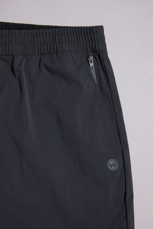 Close-up of WearEver Transit Pant, featuring an elastic waistband, zippered pocket, and small circular logo on the right side near the pocket. Shown against a neutral gray background.