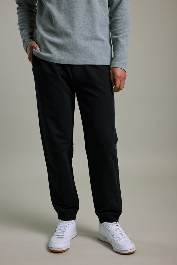 Person in Barkers Organic Classic Print Track Pant, gray sweater, and white sneakers, standing upright.