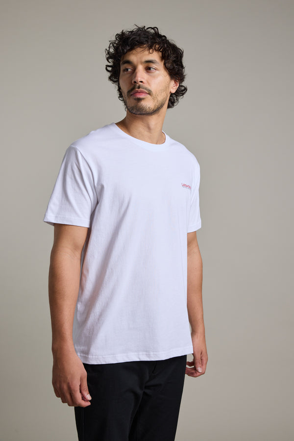 Man in Legasea Brand Tee and black pants against a neutral background.