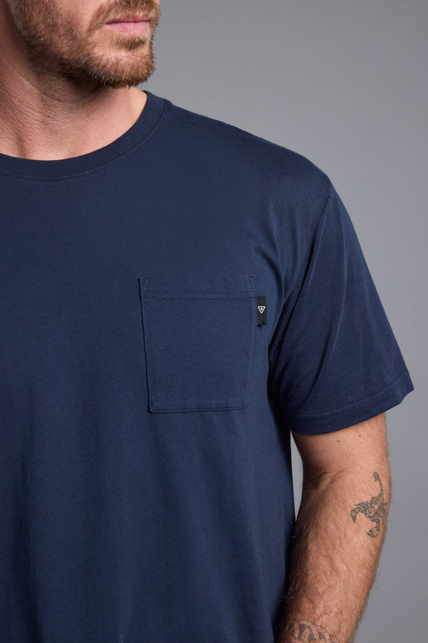A man with light facial hair wears a Barkers Summer Soul Sessions Print Tee in navy blue, featuring a chest pocket. He shows part of his face and tattooed forearm against a plain gray background.