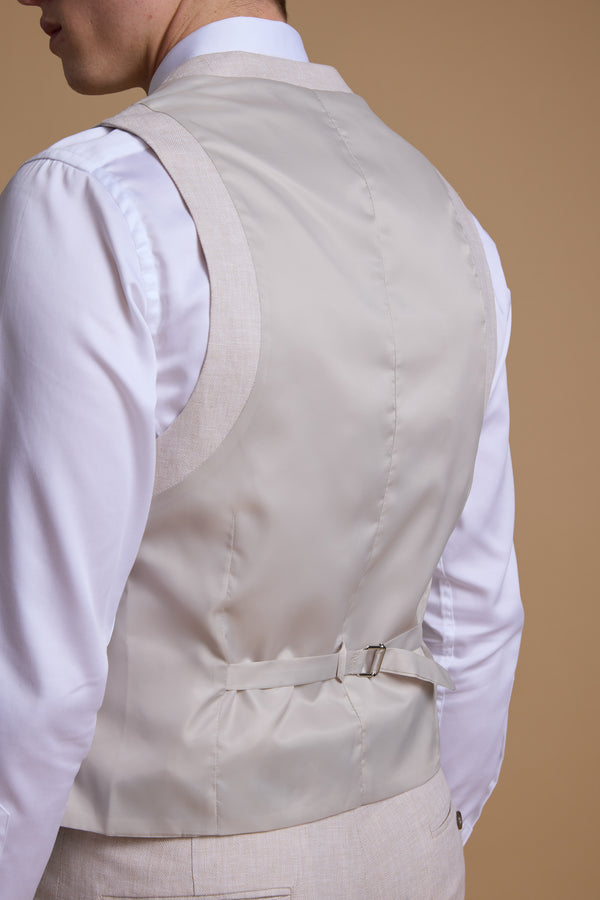 A man shown from the back wears the Barkers Somerton Texture Waistcoat—light beige linen with a satin finish and adjustable strap—over a white shirt, ideal for summer tailoring, set against a plain beige background.