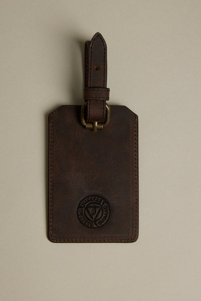 The Barkers Voyage Leather Luggage Tag, in brown with a brass buckle and embossed logo, is shown on a beige background. Visible stitching adds style—an ideal corporate gift for travelers.