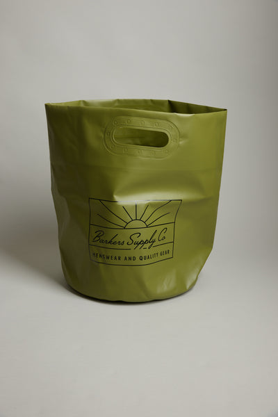 The Barkers Supply Co. Bucket is a large olive green waterproof tote with oval cut-out handles—ideal as a beach bucket for summer essentials—and features "Barkers Supply Co. Menswear and Quality Gear" printed on the front in black.