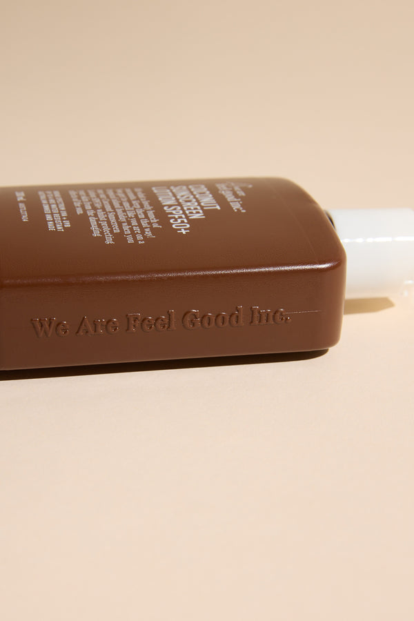 A brown plastic bottle of Other Feel Good 50+ SPF Coconut sun lotion with white text lies on its side against a beige background.