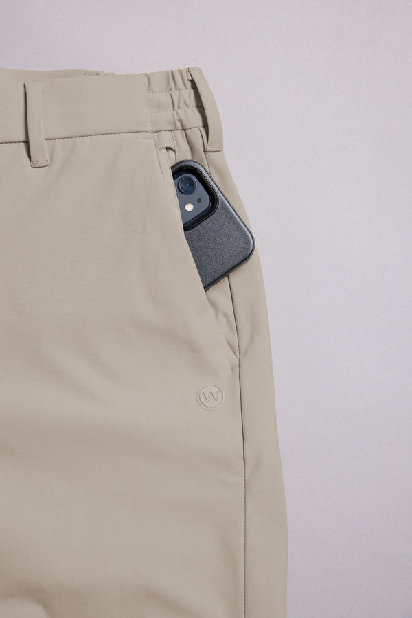 A smartphone peeks out of the front pocket of WearEver Long Game Pant travel chinos, showcasing their waistband and belt loops by WearEver against a light gray background.