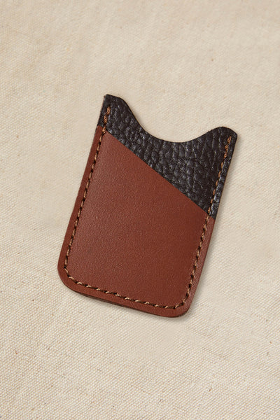 The Parisian Leather Slim Wallet by Parisian features a compact brown leather design with a darker, textured diagonal top section and matching brown stitching, displayed on a beige fabric background.
