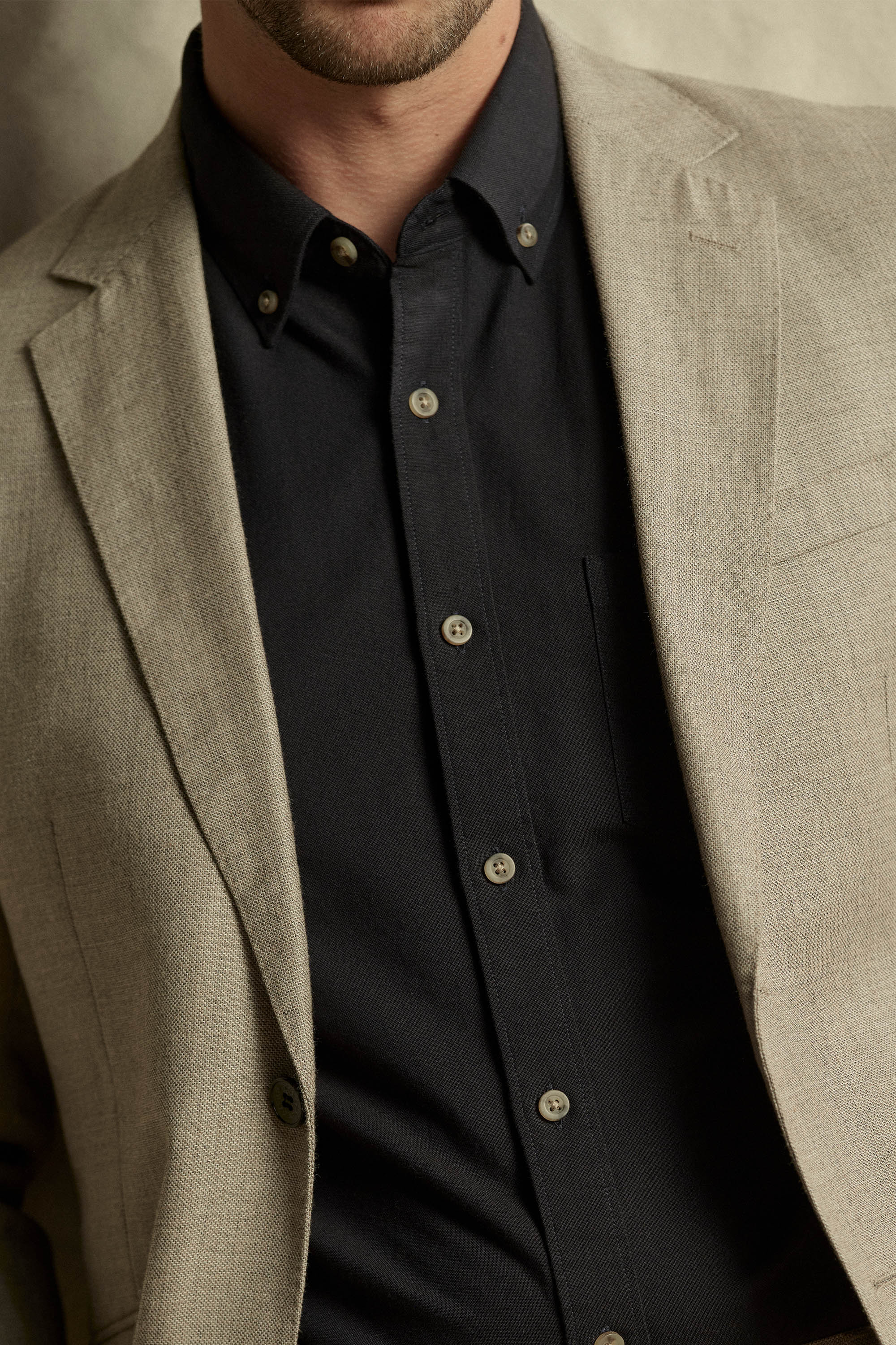 A man wears the Barkers Thatcher Oxford Shirt in tailored black, styled under a beige blazer. The image is cropped to show only his lower face, neck, and upper torso.