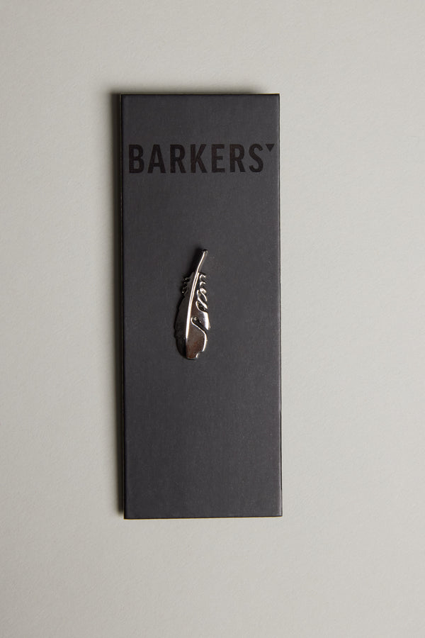 The Feather Touch Lapel Pin by Barkers features a polished silver tone feather engraved with “Story,” presented on a black card labeled Barkers and displayed on a light grey surface.