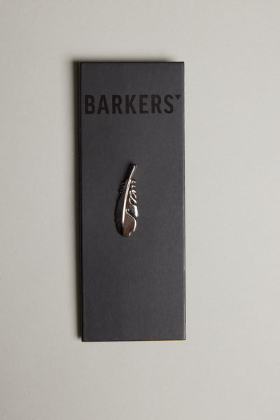 The Feather Touch Lapel Pin by Barkers features a polished silver tone feather engraved with “Story,” presented on a black card labeled Barkers and displayed on a light grey surface.