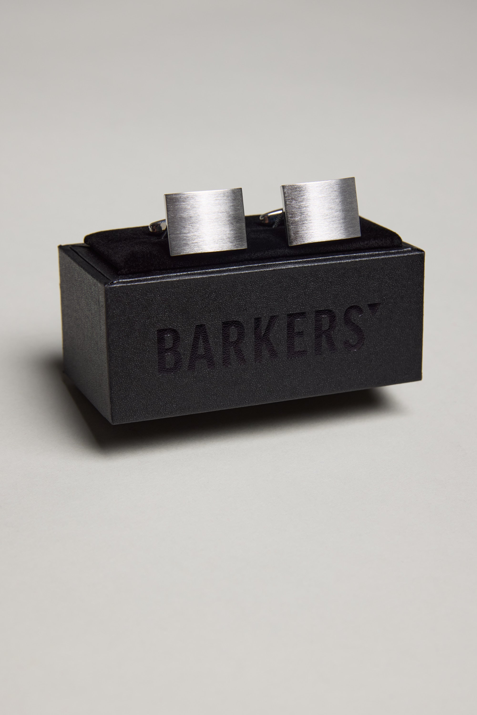 The Classic Brushed Silver Rectangle Cufflink by Barkers is displayed on a black box with the brand name in bold, standing out against a plain light grey background. Ideal for French Cuff Shirts.