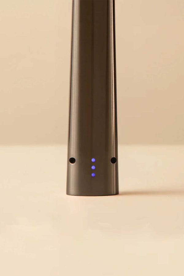 A close-up of the Flint Rechargeable Lighter 2.0 by Flint, a sleek metallic USB-C lighter with four blue LED lights and two small holes near its base, stands upright on a plain light beige background.