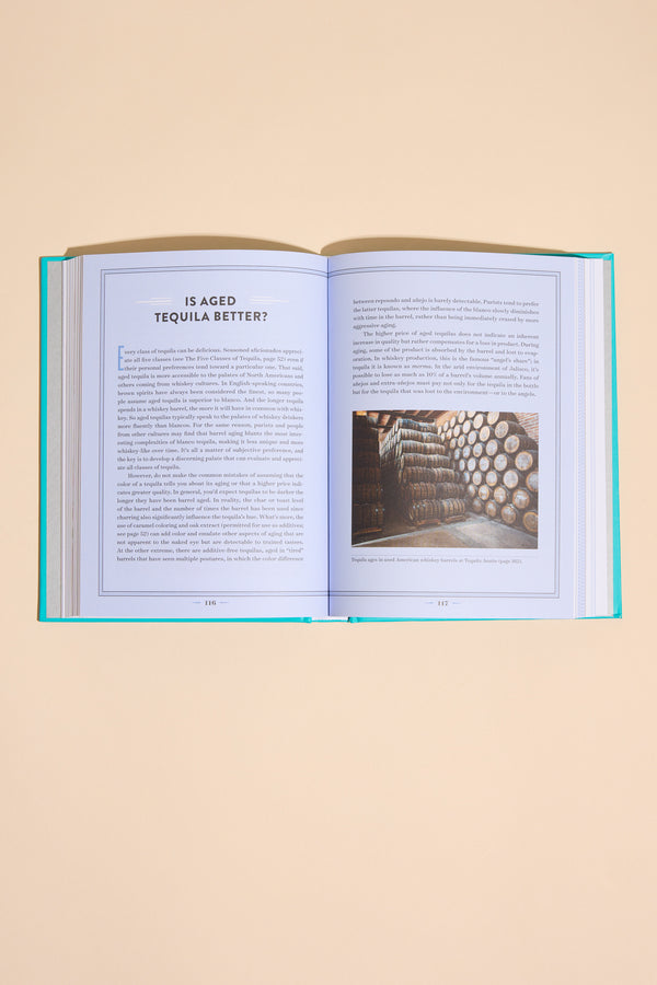 An open copy of "A Field Guide To Tequila" by Other rests on a beige surface, opened to the section "Is Aged Tequila Better?" with text and a storeroom barrels photo displayed across both pages.