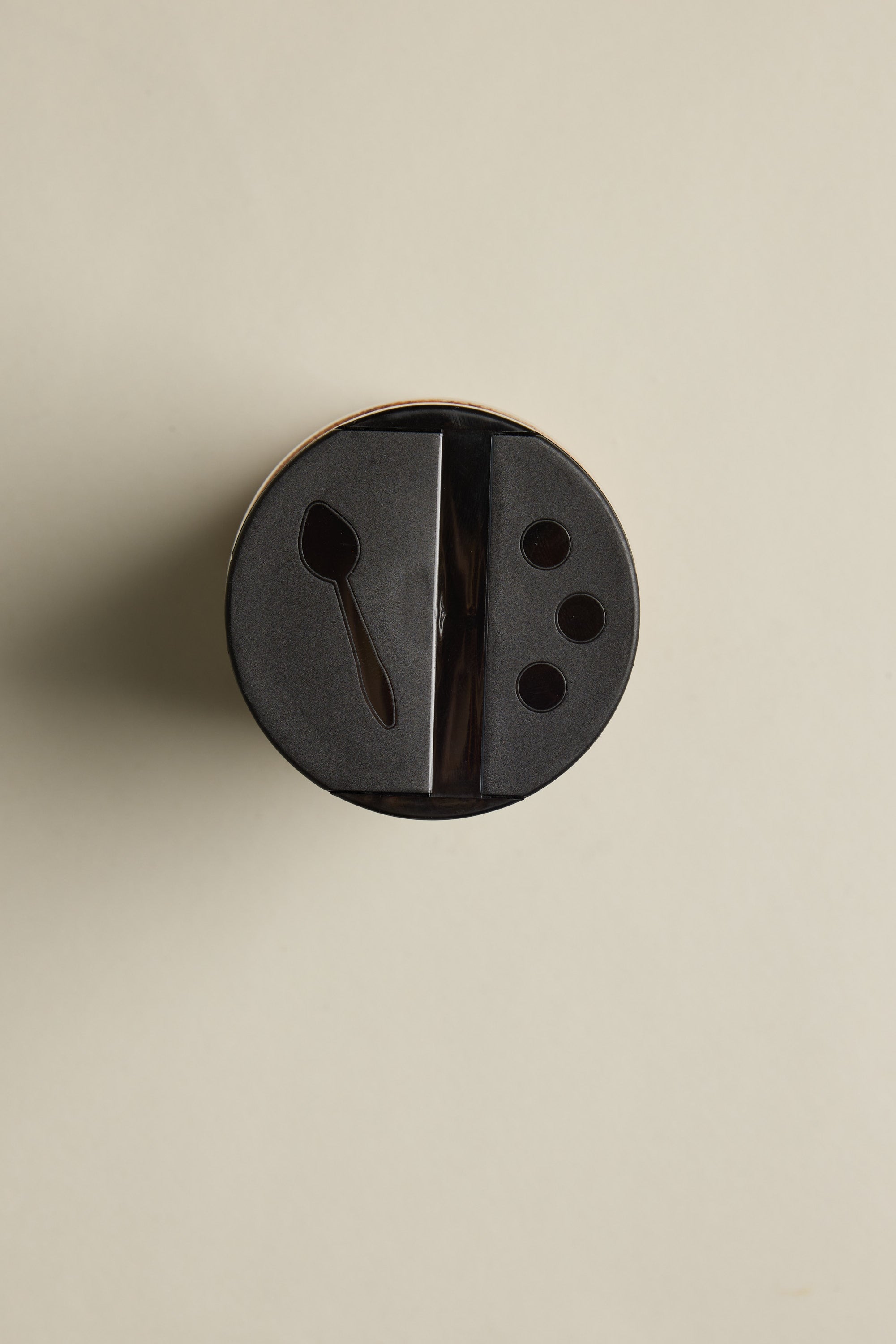 A black plastic lid on The Pork Rub 295g by Other, viewed from above, with a spoon-shaped slot and three small holes—ideal for sprinkling BBQ seasoning or smoked paprika—set against a plain light background.