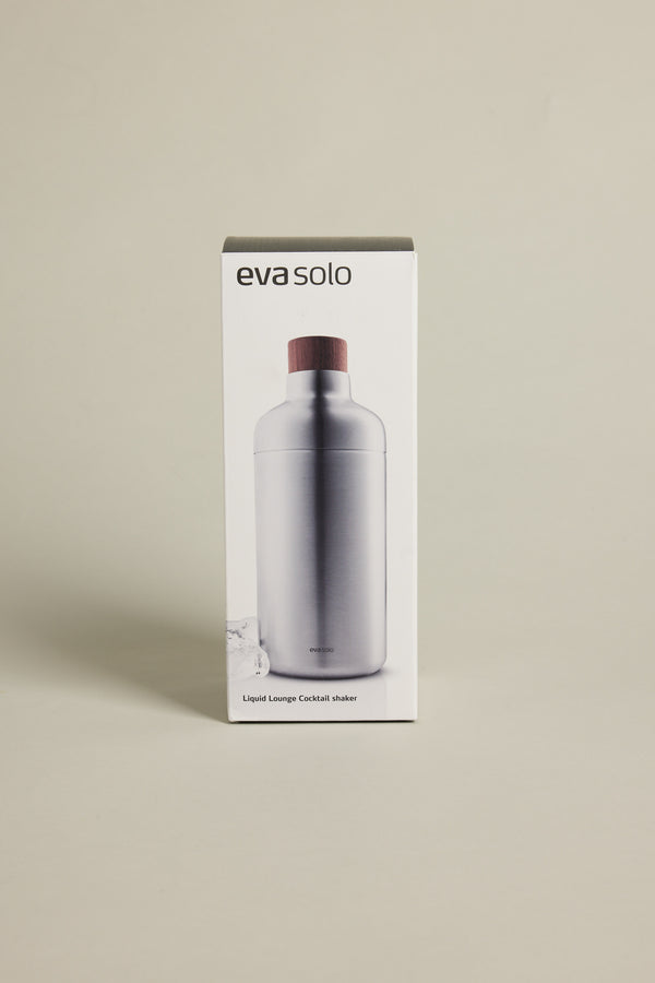 A box featuring the Other brand displays a sleek, stainless steel Liquid Lounge Cocktail Shaker with a wooden top on a plain, light background—an essential addition to any home bar.