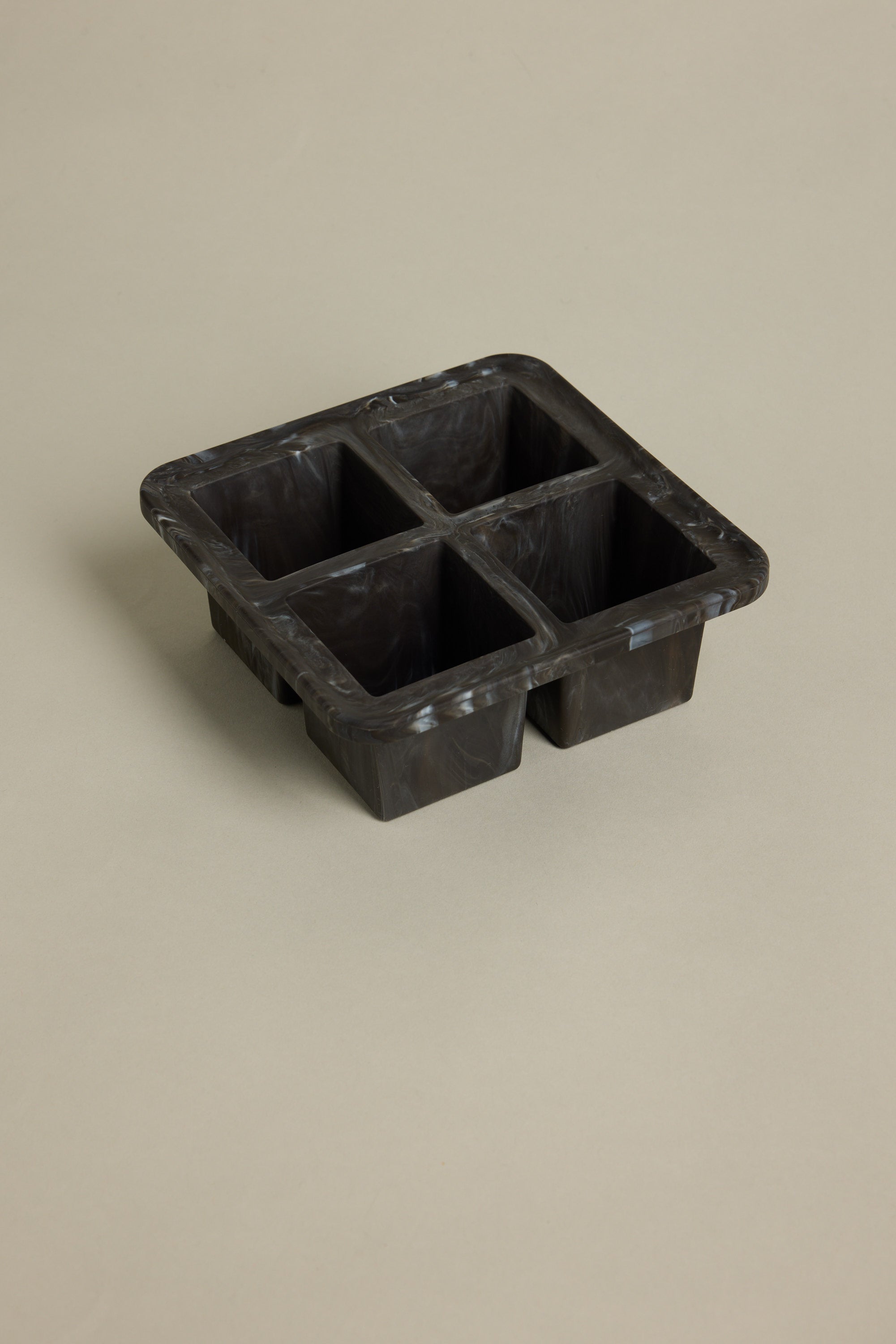 The Other Ice Tray Sphere Marble Black features four deep compartments for slow-melting ice cubes and sits elegantly on a light beige surface—an ideal addition to any home bar.