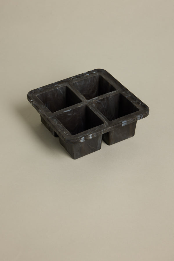 The Other Ice Tray Sphere Marble Black features four deep compartments for slow-melting ice cubes and sits elegantly on a light beige surface—an ideal addition to any home bar.