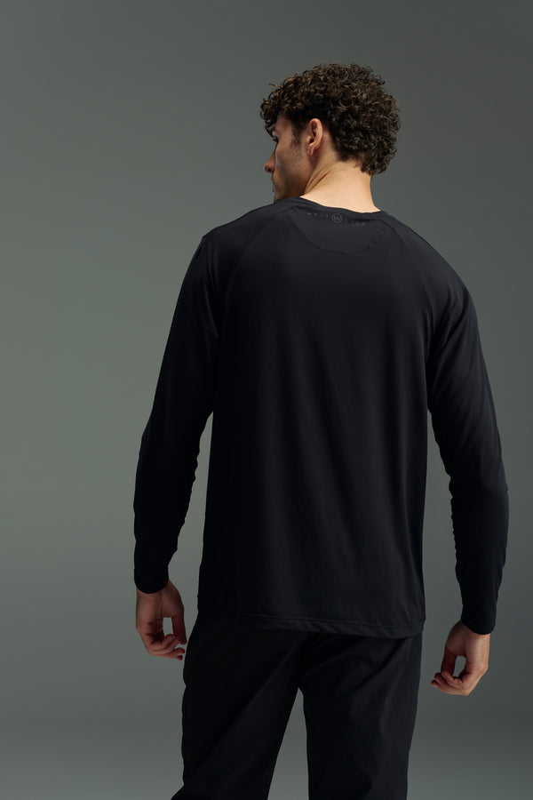 A man with curly hair, seen from behind, wears the WearEver Pulse Long Sleeve Tee in black and matching black pants against a plain gray background.