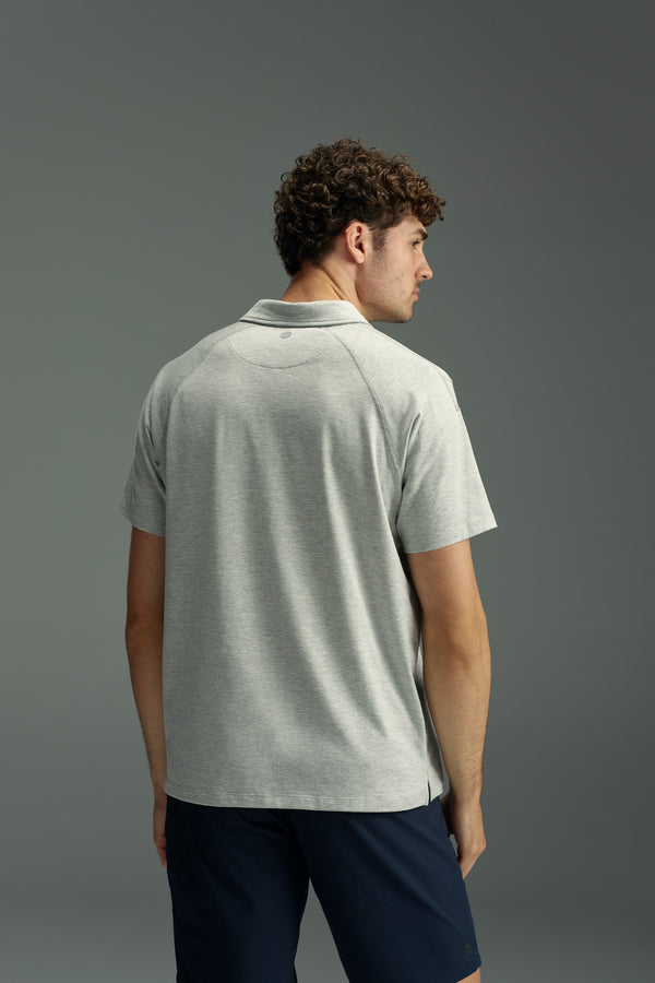 A man with curly hair is seen from behind wearing a WearEver Outbound Polo in light gray, made from breathable cotton-blend fabric, paired with dark shorts against a plain gray background.